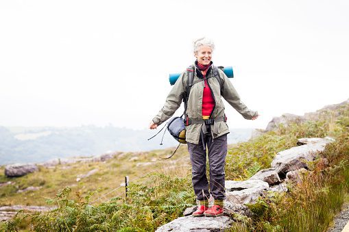 Older woman happily trekking in the mountains of ireland, solo travelor enjoying freedom and independence.