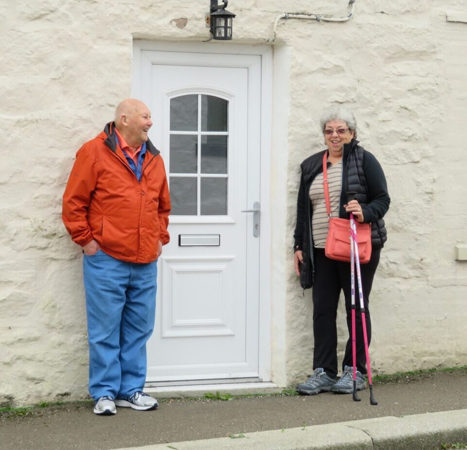 A man and woman with a walking sticks standing in front of a white door
