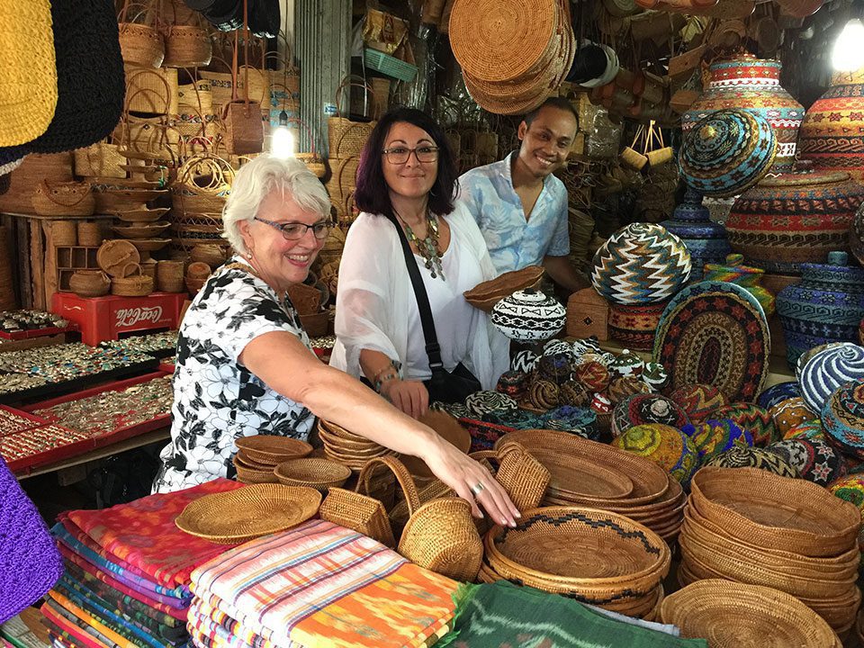 Two woman and young man look at goods in Bali marketplace