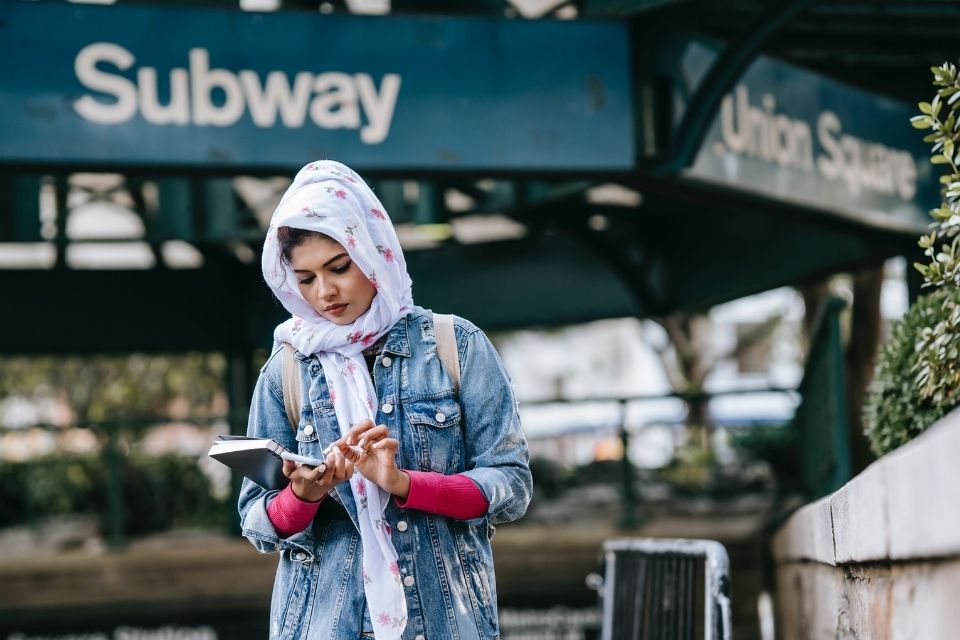 Young woman wearing head covering stands in front of subway