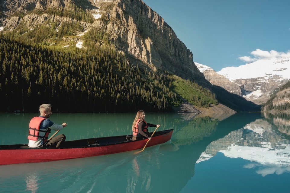 Paddlers take one of the signature red rental canoes on Lake Louise, with Mt. Victoria in the foreground. Fairmont Chateau Lake Louise