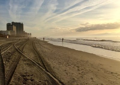 Track marks along the sand of a beach, with buildings in the distance