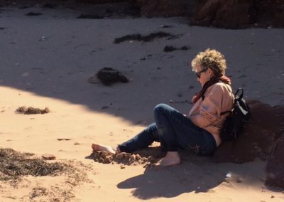 A woman sits in the sand, looking out towards the water