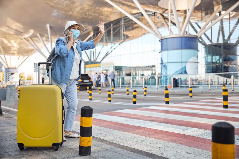 Elderly female tourist with a cellphone in one hand hailing a cab in the street