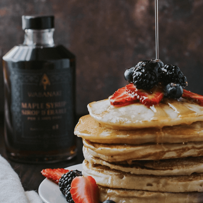 A stack of pancakes with Neqotkuk Tobique First Nation maple syrup being poured on top.