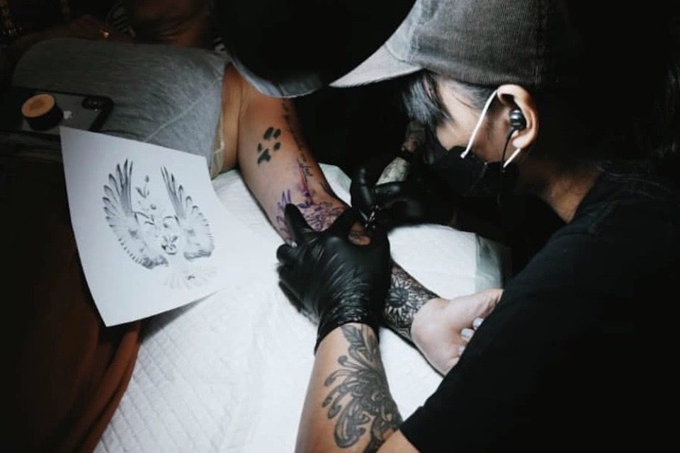 A tattoo artist works on a tattoo of a hawk