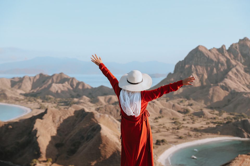A woman in a red dress holds her arms up happy midlife