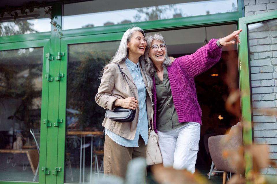 Two older women friends laugh together while one points to something in the distance