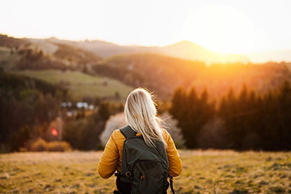 Rear view of senior woman walking outdoors in nature at sunset, hiking.