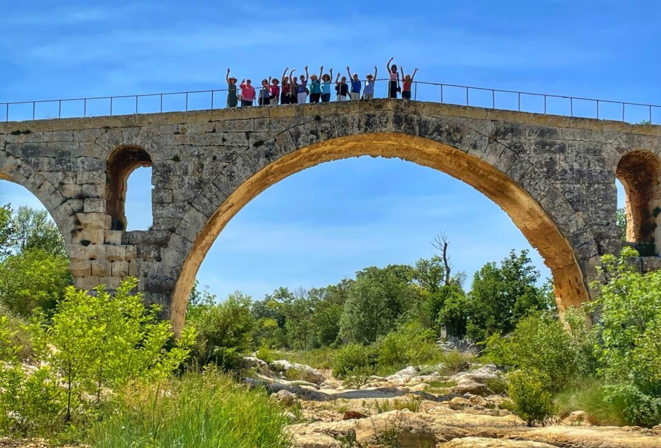 A group of women stand and wave to the camera on a bridge in Pont Julien