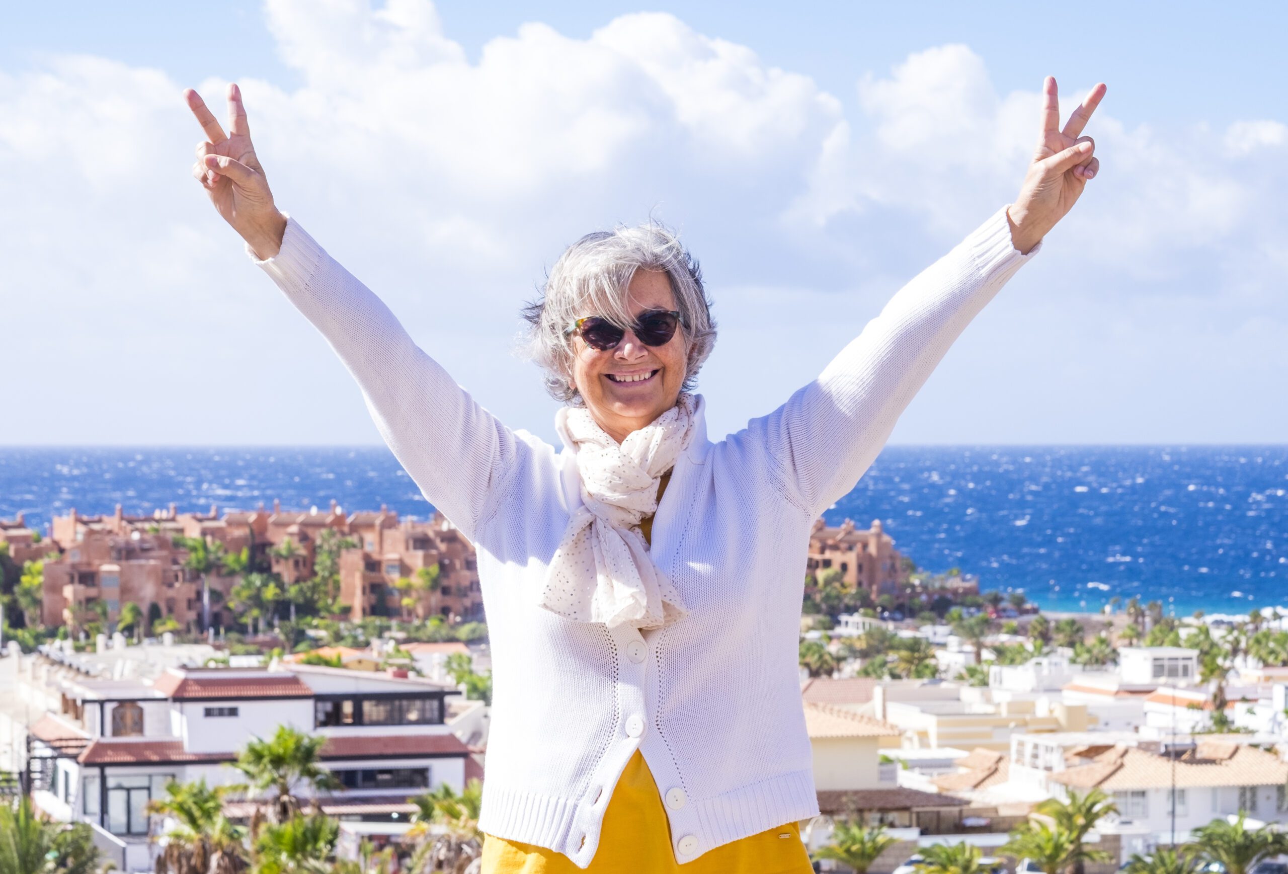 Happy senior woman enjoying sea holiday in winter. Positive, optimistic active retiree smiling with arms up