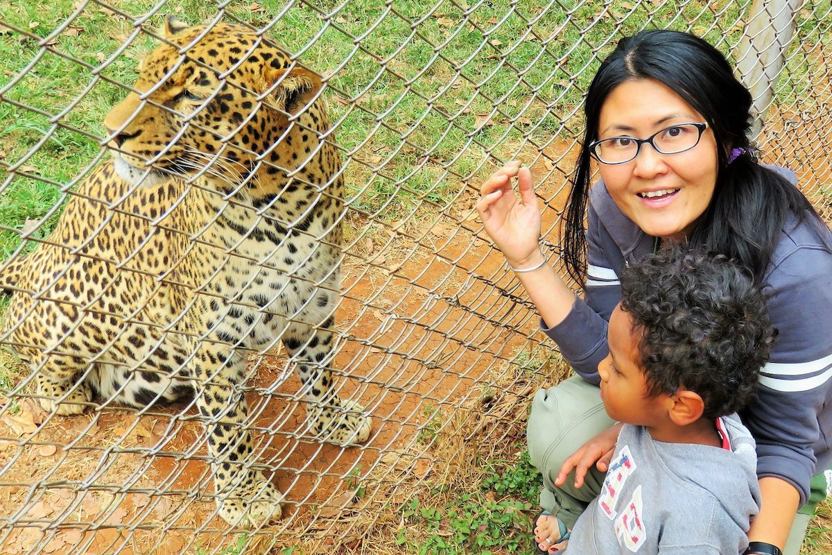 A woman and young child next to a leopard behind a fence in Kenya