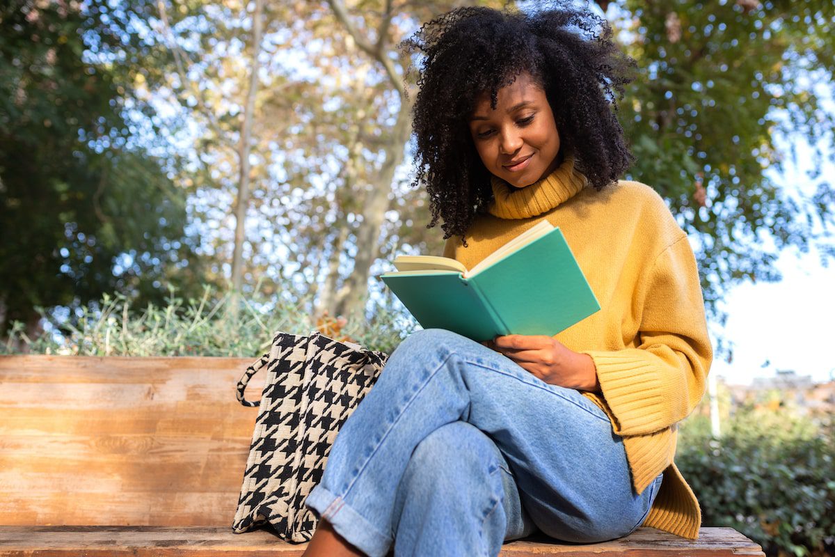 A woman sits and reads a book in a park