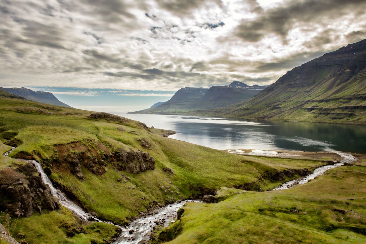 green rolling hills next to the ocean with cloudy skies