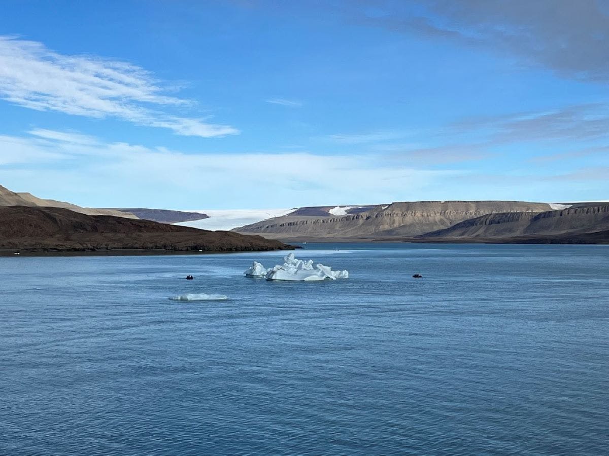 image of an iceberg floating in the middle of the ocean with mountains in the background
