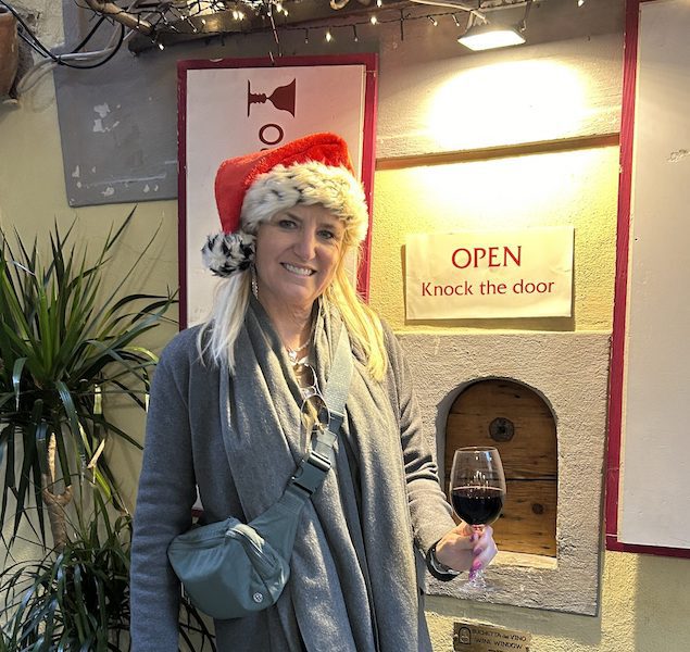 A woman stands next to a wine window in Florence, holding a glass of wine.