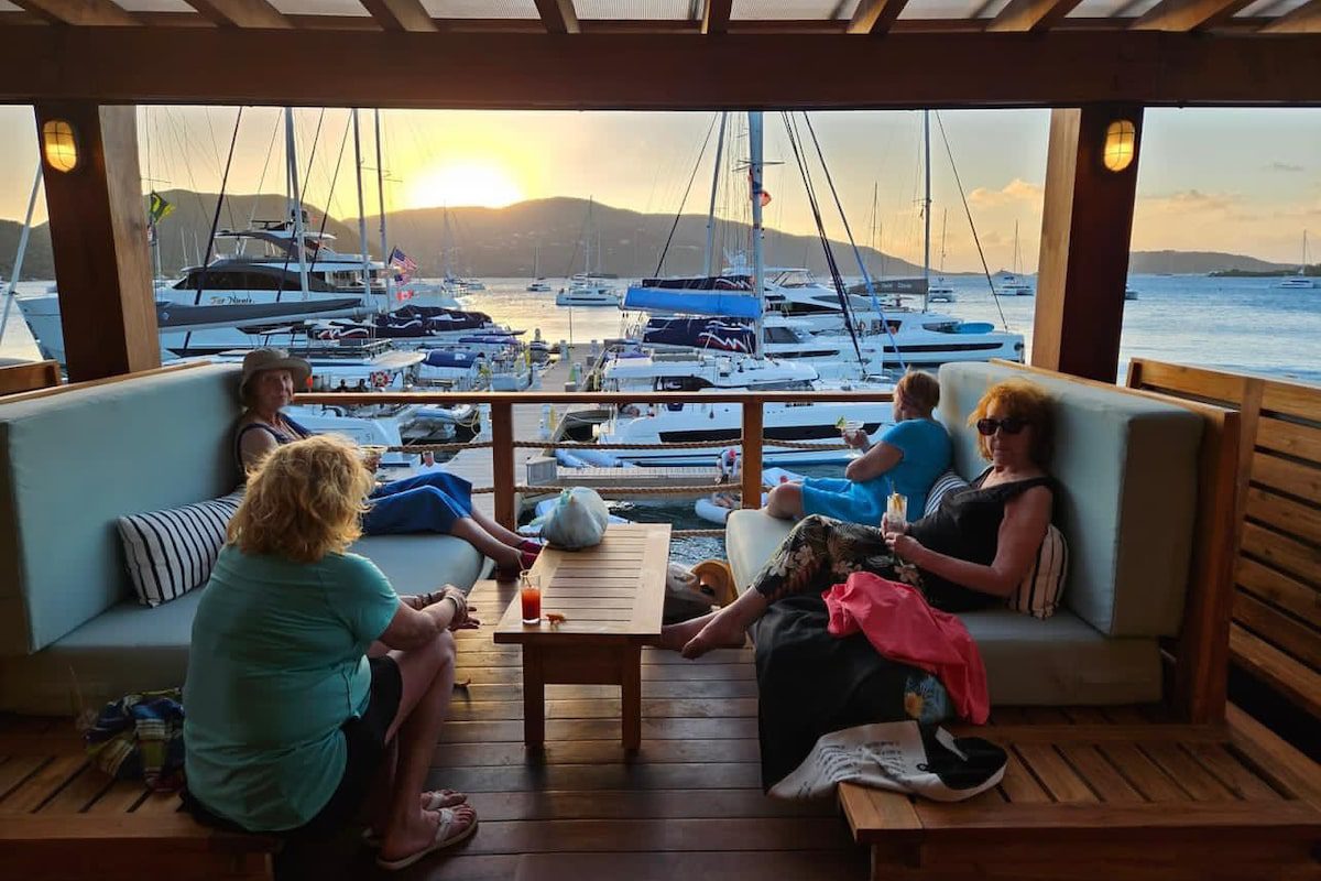 A group of women enjoying happy hour at a beach bar in the British Virgin Islands, on a sailing for seniors trip.