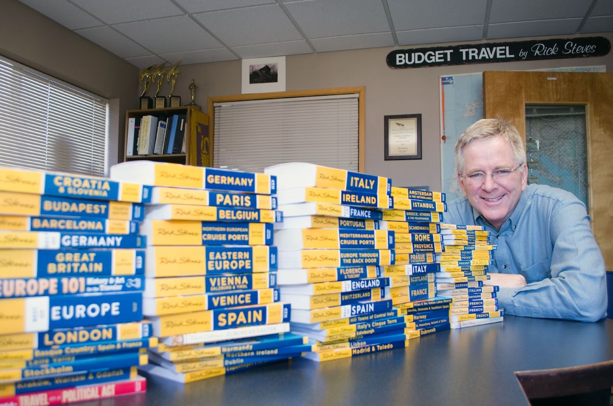 Rick Steves next to his stacks of guidebooks on traveling Europe
