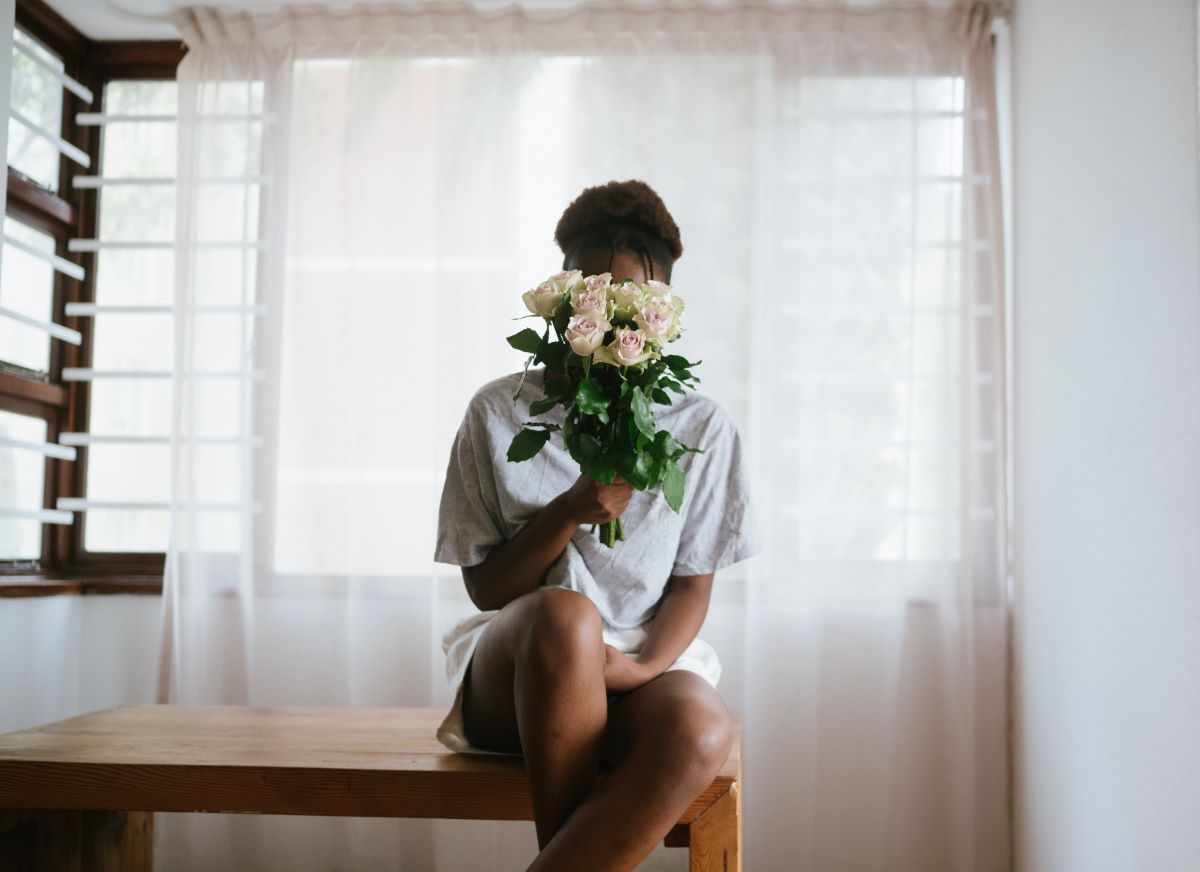 Woman sitting in the middle of a room holding a bunch of white roses in front of her face