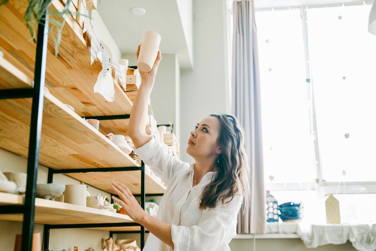 A woman reaching to place a cup on a shelf in her home to start downsizing for travel