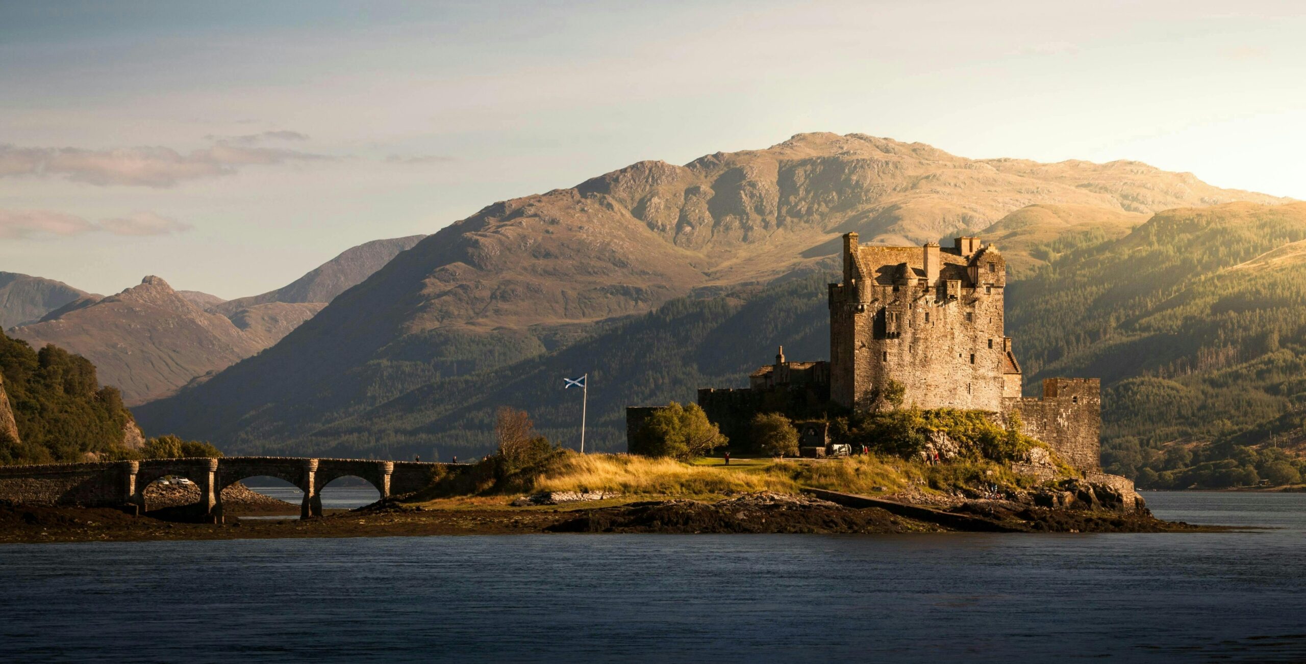 scottish castle standing along the lake with rolling hills in the background