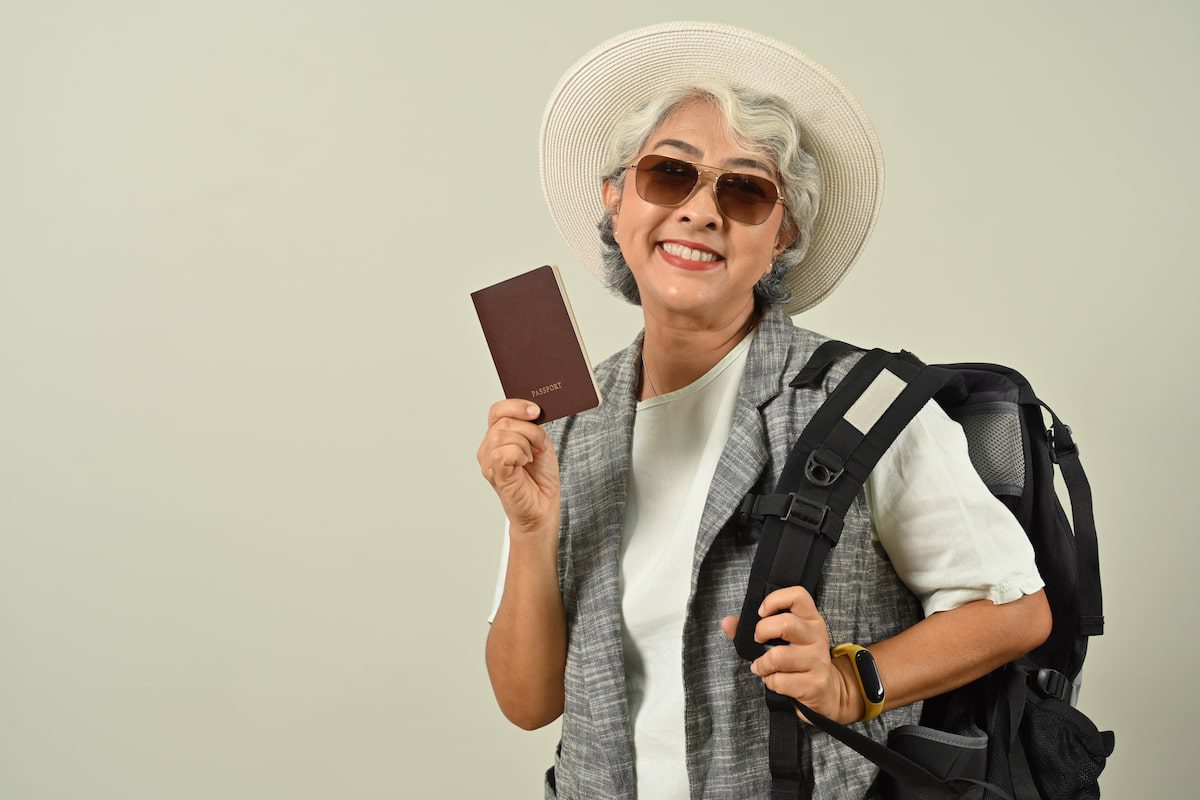 Happy mature woman tourist woman 50+ solo travel holding passport on gray background Women Over 50 Who Love Solo Travel