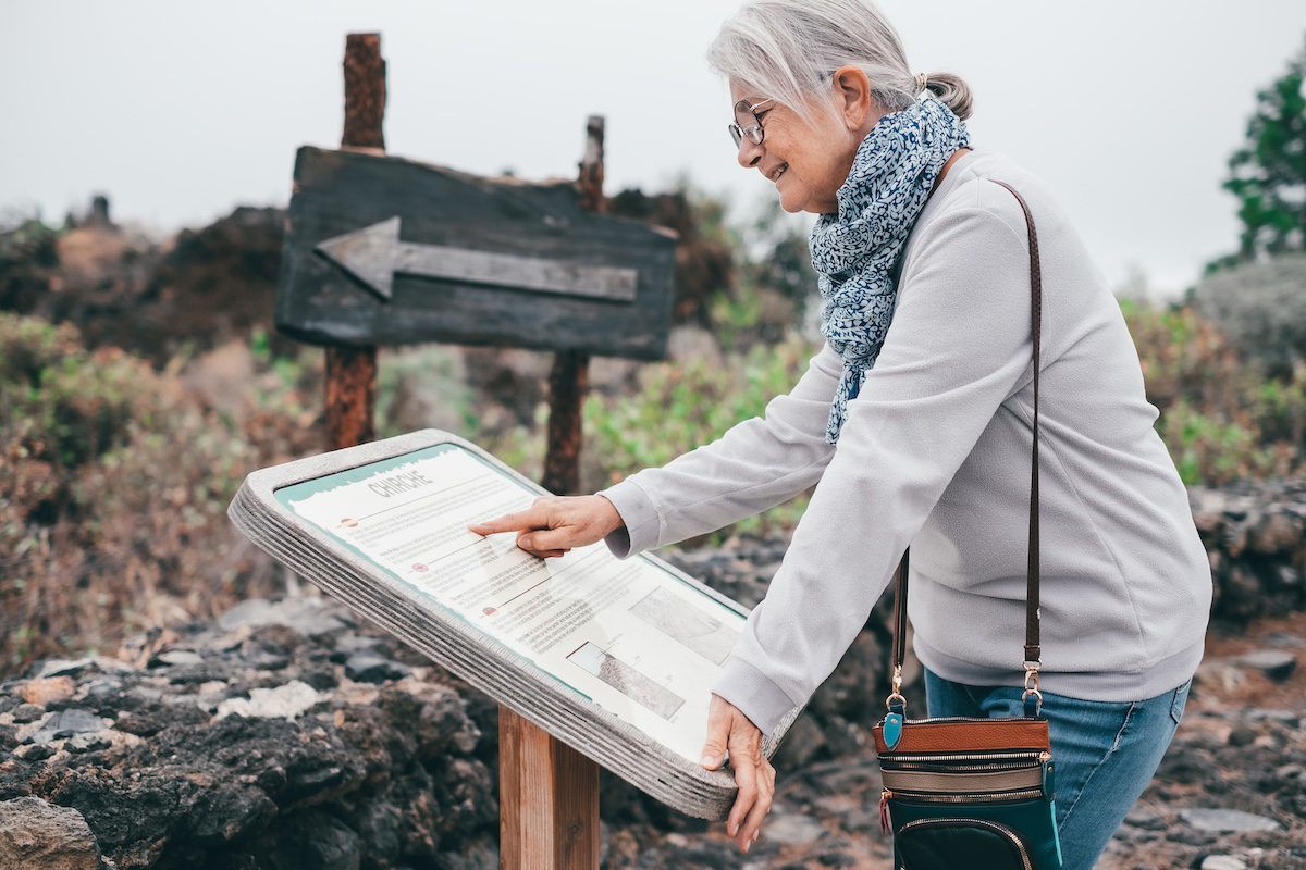 Smiling elderly woman visiting the island of Tenerife reads tourist information of the Chirche mountain area.