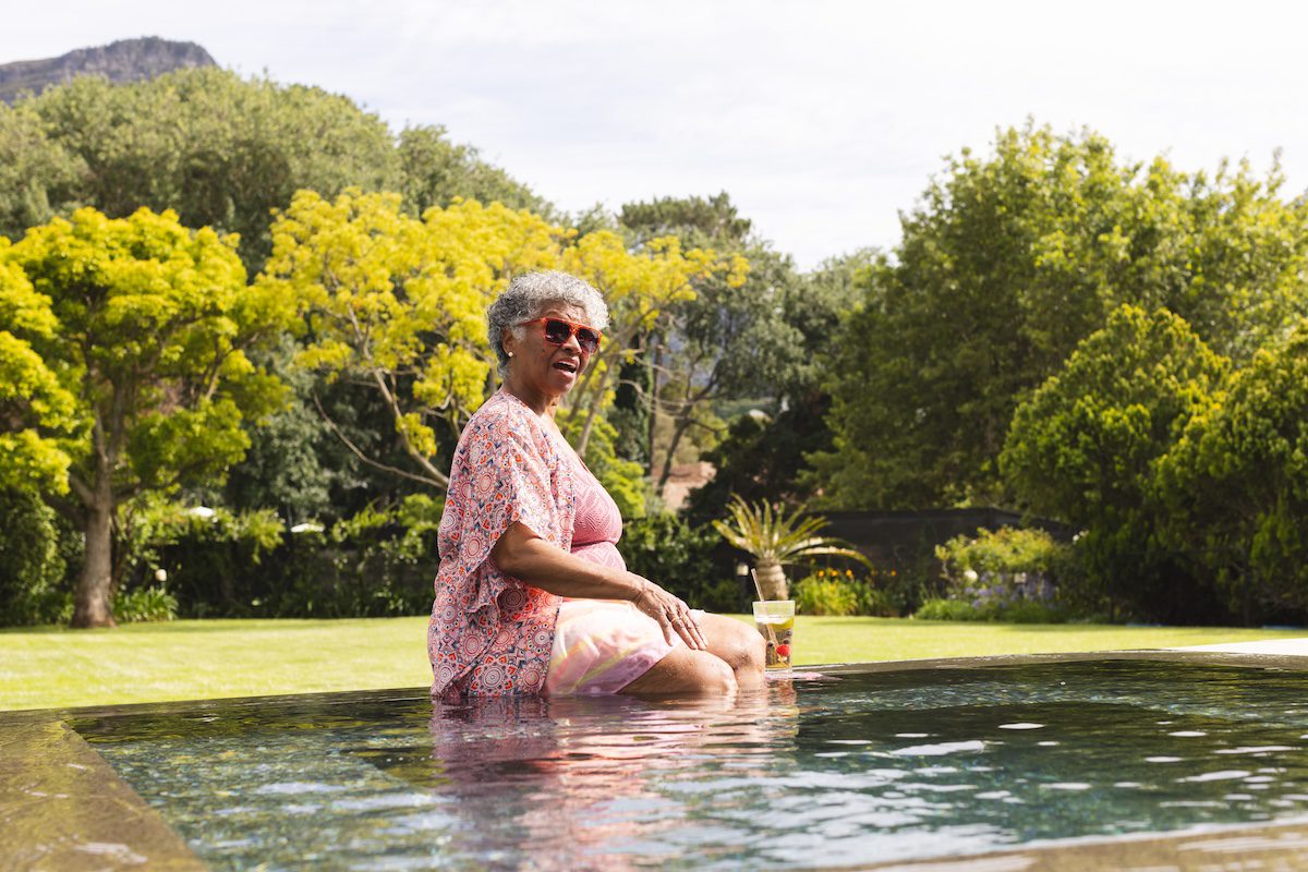 A woman enjoys a refreshing drink next to the pool on a solo wellness retreat for women.