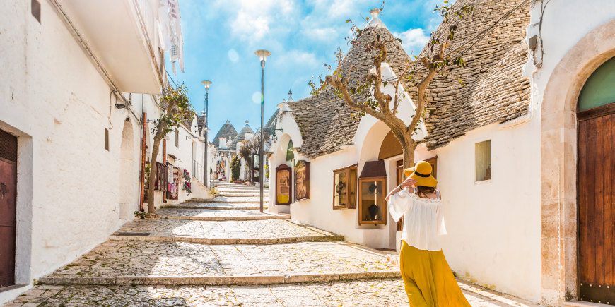 A woman in a flowing yellow skirt and had walks alone on a street in Fasano, a stop on the Discover Puglia tour by Just You.