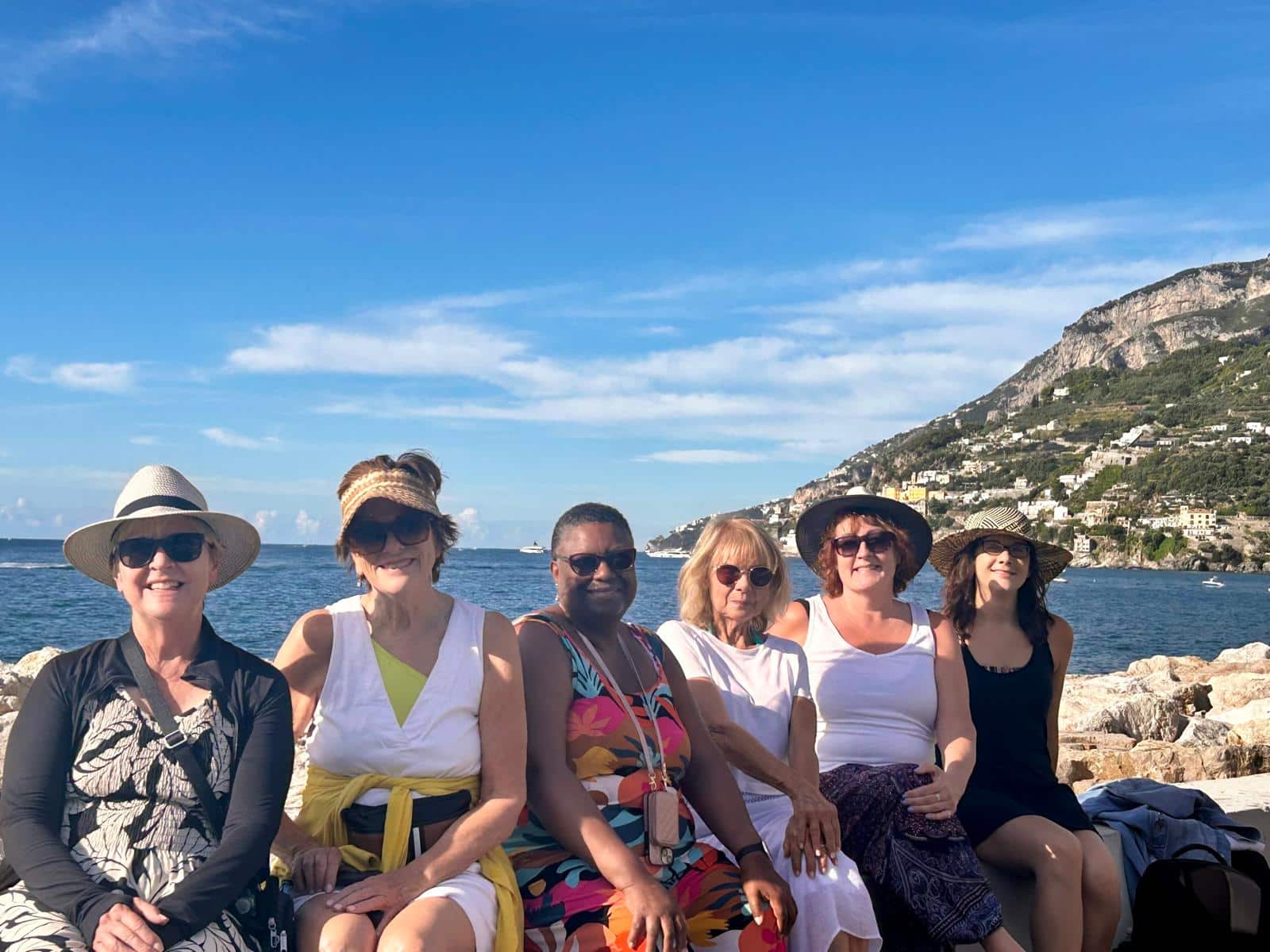A diverse group of women on tour with Women Travel Abroad pose for a shot with the ocean and mountains in the background.